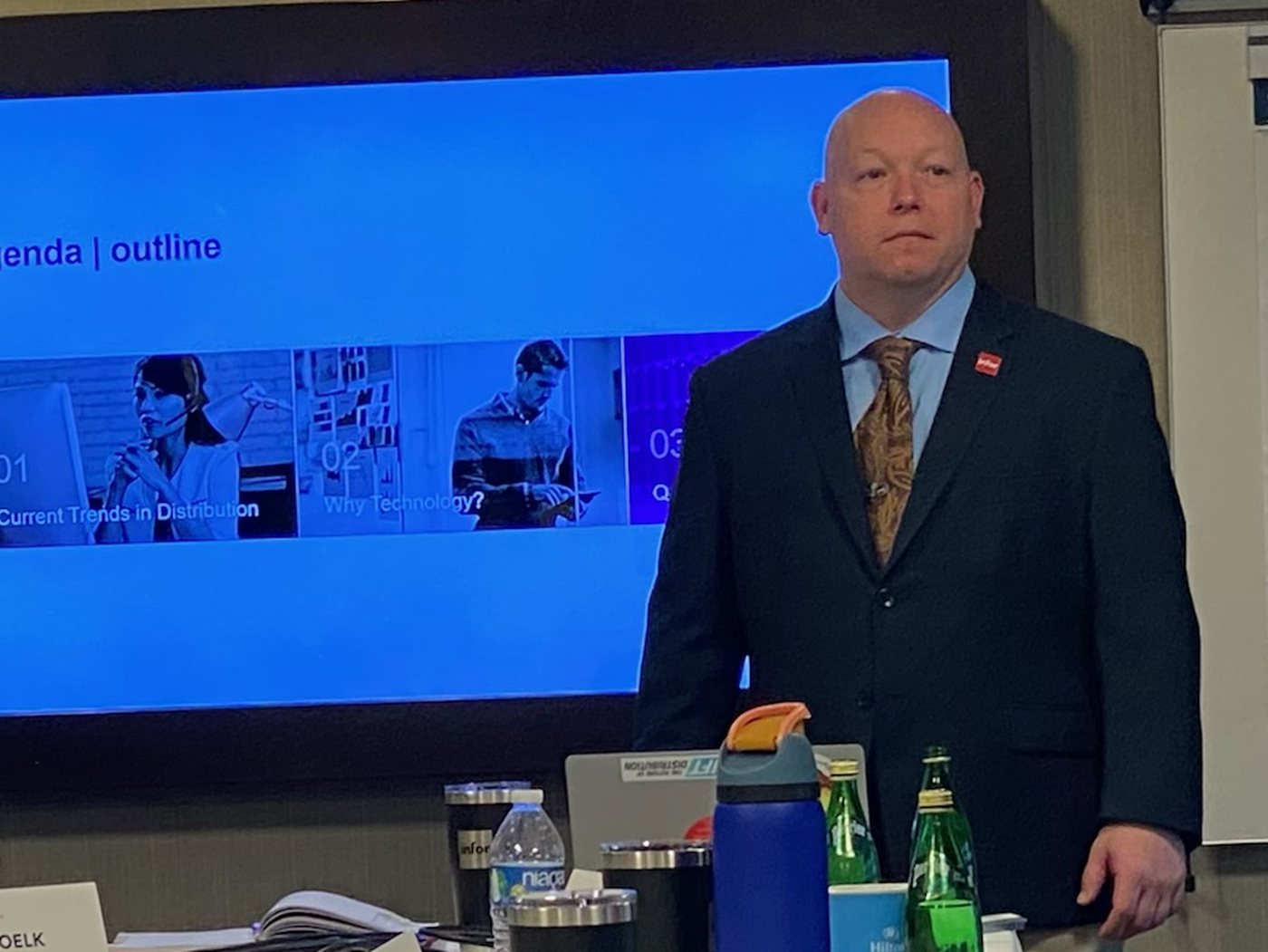 Will Quinn presenting to a distribution executive roundtable, a slide reading Current Trends in Distribution on the screen behind him